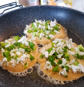three pikelets in a pan covered in angled onion leaves and flowers